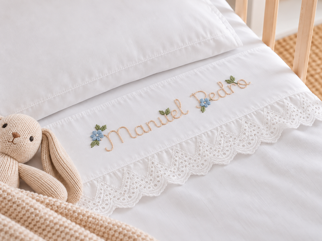 Lençol branco de berço com nome personalizado, flores azuis bordadas e remate rendilhado